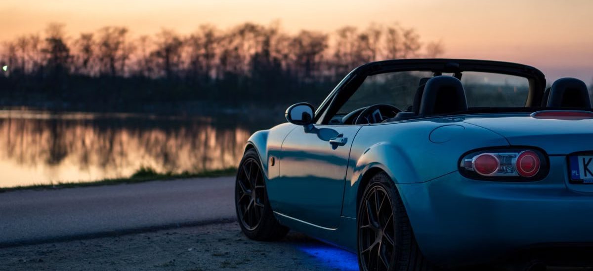 A sports car parked by a lake at sunset in Brzegi, Poland, offering a scenic view.