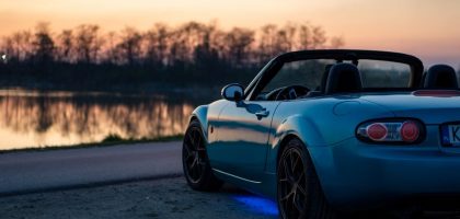 A sports car parked by a lake at sunset in Brzegi, Poland, offering a scenic view.
