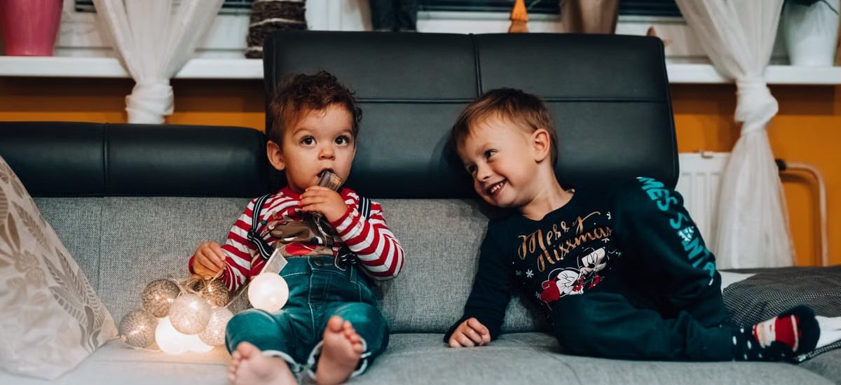 Two young boys with festive lights sitting on a couch, enjoying the holiday spirit indoors.