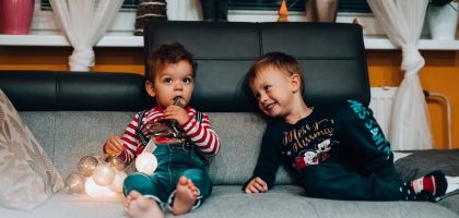 Two young boys with festive lights sitting on a couch, enjoying the holiday spirit indoors.
