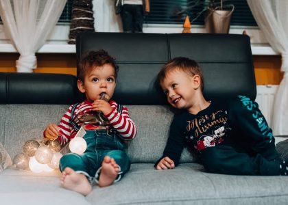 Two young boys with festive lights sitting on a couch, enjoying the holiday spirit indoors.