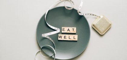 Flat lay of scrabble tiles spelling 'eat well' on a plate with a tape measure, promoting healthy eating.