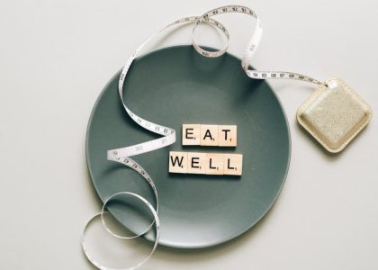 Flat lay of scrabble tiles spelling 'eat well' on a plate with a tape measure, promoting healthy eating.